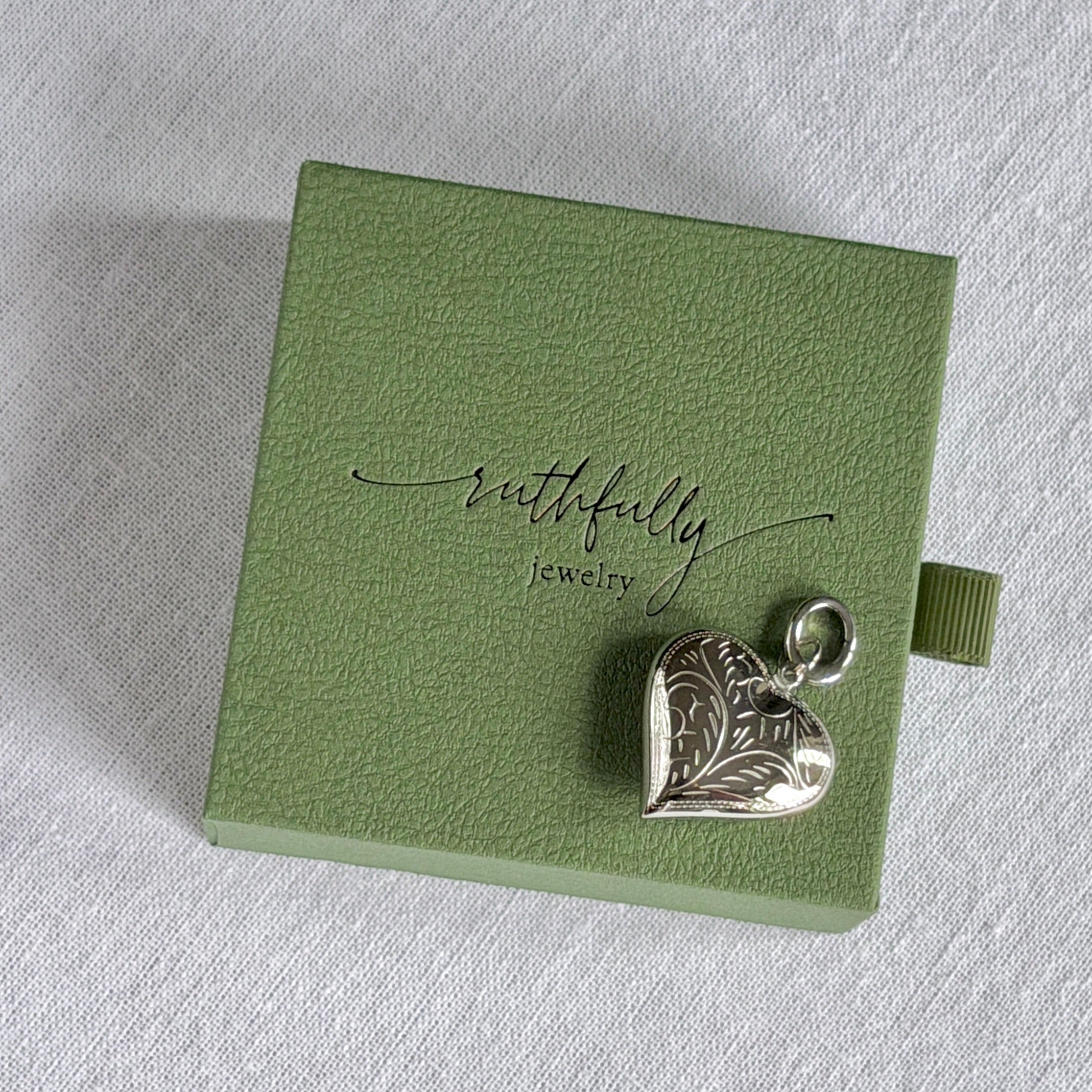Silver heart-shaped pendant on a green jewelry box with 'ruthfully jewelry' branding.